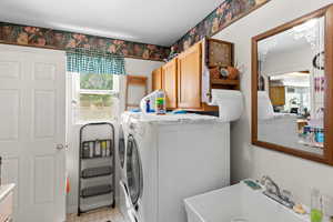 Laundry area featuring cabinet space, washing machine and clothes dryer, and wallpapered walls