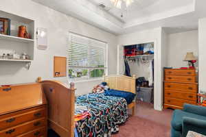 Carpeted bedroom featuring a tray ceiling and a closet