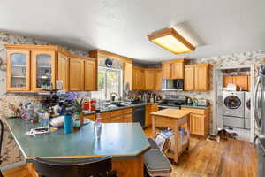 Kitchen with wallpapered walls, washer and dryer, light wood finished floors, a peninsula, and appliances with stainless steel finishes