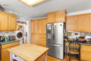 Kitchen featuring wallpapered walls, stainless steel fridge, built in study area, light wood finished floors, and washer / clothes dryer
