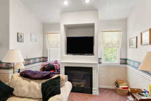 Carpeted living area featuring wallpapered walls, a wainscoted wall, a glass covered fireplace, and recessed lighting