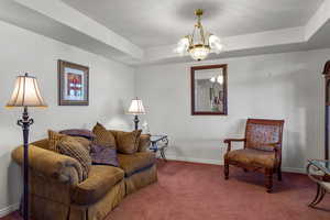 Carpeted living area featuring a chandelier and a raised ceiling