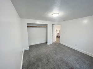 Unfurnished bedroom featuring a textured ceiling, a closet, and dark colored carpet