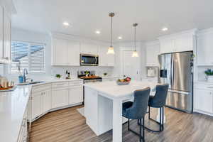 Kitchen featuring appliances with stainless steel finishes, white cabinetry, a breakfast bar area, a kitchen island, and light wood-type flooring