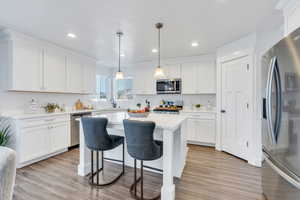 Kitchen with stainless steel appliances, white cabinets, a kitchen bar, light countertops, and recessed lighting