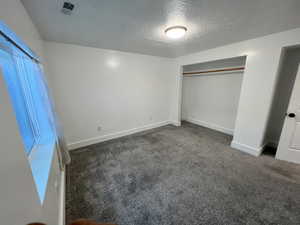 Unfurnished bedroom with a textured ceiling, carpet floors, and a closet