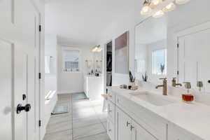 Full bathroom with two vanities, a chandelier, a tub to relax in, tile patterned floors, and a spacious closet