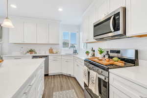 Kitchen featuring stainless steel appliances, recessed lighting, light countertops, white cabinets, and light wood-style flooring