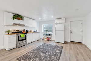 Kitchen featuring stainless steel electric range oven, freestanding refrigerator, light wood-style flooring, white cabinets, and recessed lighting