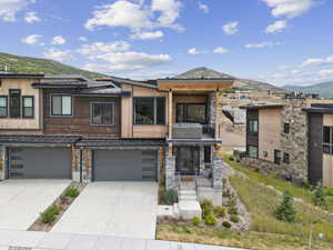 View of front facade featuring a mountain view, a balcony, a standing seam roof, a metal roof, and driveway