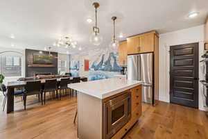 Kitchen with stainless steel appliances, open floor plan, light wood finished floors, light countertops, and light brown cabinetry