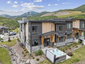Contemporary home with stone siding, a hot tub, a mountain view, a chimney, and a standing seam roof