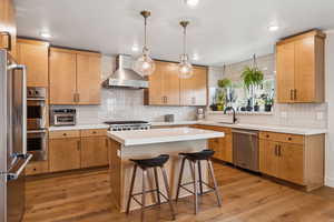 Kitchen with light wood finished floors, tasteful backsplash, stainless steel appliances, wall chimney exhaust hood, and light countertops