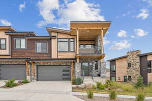 Contemporary home featuring a balcony, concrete driveway, a garage, and stone siding