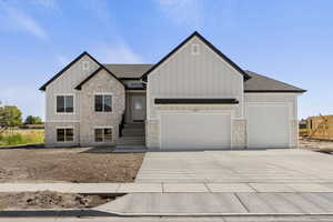 View of front of house featuring stone siding, board and batten siding, a shingled roof, and concrete driveway