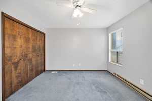 Unfurnished bedroom featuring baseboard heating, carpet, a closet, a ceiling fan, and a textured ceiling