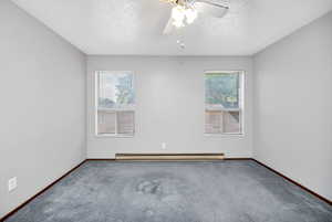 Carpeted spare room featuring plenty of natural light, a textured ceiling, ceiling fan, and baseboard heating