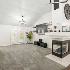 Living area featuring a tiled fireplace, light carpet, vaulted ceiling, and a chandelier
