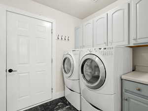 Laundry room off the garage, with cabinet space, dark marble finish floors, and a textured ceiling