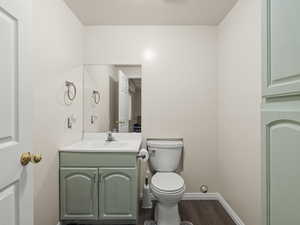 Half bathroom attached to bedroom 3 in basement, with wood finished floors and vanity and additional storage cabinet
