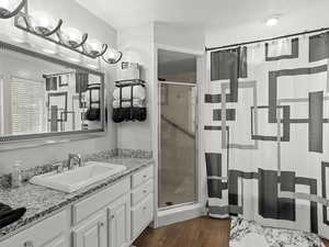 Full primary bathroom with a stall shower, separate tub, grab bars in both shower and tub, vanity, and wood finished floors