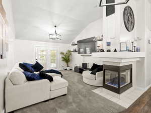 Carpeted living room with lofted ceiling, a chandelier, and 3-sided gas fireplace