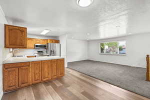 Kitchen featuring light countertops, stainless steel appliances, open floor plan, brown cabinets, and light wood-style flooring