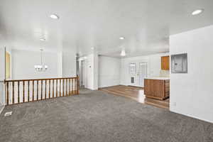 Unfurnished living room featuring carpet, a chandelier, recessed lighting, electric panel, and wood finished floors