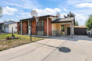 View of front facade featuring driveway, brick siding, a chimney, and an attached carport