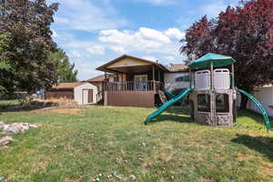 Rear view of property with a playground, a storage unit, and a yard
