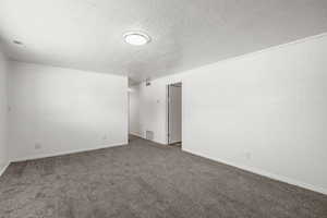 Carpeted empty room featuring a textured ceiling and baseboards
