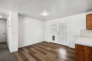 Unfurnished dining area with dark wood-style floors, french doors, and a textured ceiling