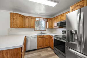 Kitchen featuring appliances with stainless steel finishes, brown cabinetry, light wood finished floors, a textured ceiling, and light countertops