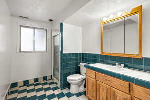 Bathroom featuring a textured ceiling, tile patterned floors, a stall shower, vanity, and wainscoting