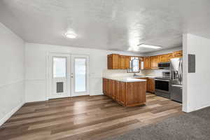 Kitchen with brown cabinets, a peninsula, a textured ceiling, wood finished floors, and stainless steel appliances