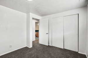 Unfurnished bedroom with dark carpet, a closet, and a textured ceiling