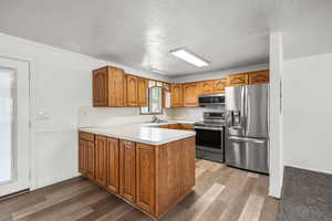 Kitchen with appliances with stainless steel finishes, a peninsula, brown cabinets, light countertops, and wood finished floors