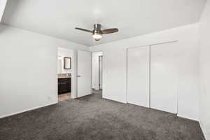 Unfurnished bedroom featuring carpet flooring, a closet, ensuite bathroom, and ceiling fan