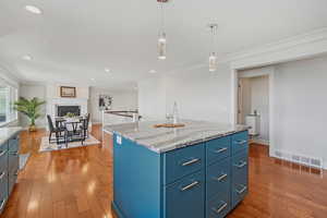Kitchen with blue cabinets, light wood-style flooring, hanging light fixtures, recessed lighting, and crown molding