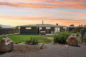 Back of house at dusk with a fenced backyard, brick siding, a patio, and a chimney