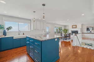 Kitchen featuring blue cabinetry, hardwood / wood-style floors, a center island, hanging light fixtures, and light stone countertops