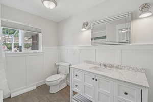 Bathroom featuring baseboard heating, vanity, a decorative wall, a wainscoted wall, and wood finished floors