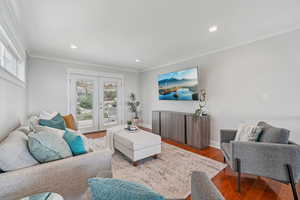 Living area with plenty of natural light, crown molding, wood finished floors, recessed lighting, and french doors