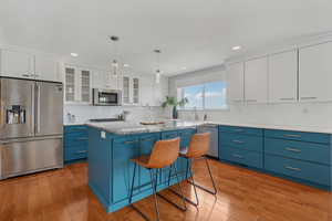Kitchen featuring blue cabinetry, stainless steel appliances, light wood-style flooring, backsplash, and recessed lighting
