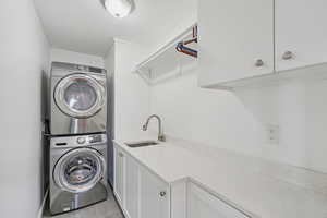 Washroom with stacked washer / drying machine, cabinet space, and light wood-style flooring