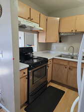 Kitchen featuring stainless steel range with electric stovetop, light wood finished floors, under cabinet range hood, light countertops, and white fridge