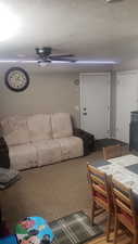Carpeted living area with a ceiling fan and a textured ceiling
