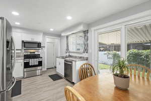 Kitchen featuring appliances with stainless steel finishes, light wood-style floors, white cabinets, decorative backsplash, and recessed lighting