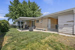 Back of house featuring a lawn, a patio area, and brick siding