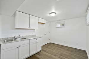 Kitchen featuring white cabinetry, wood finished floors, and light stone countertops